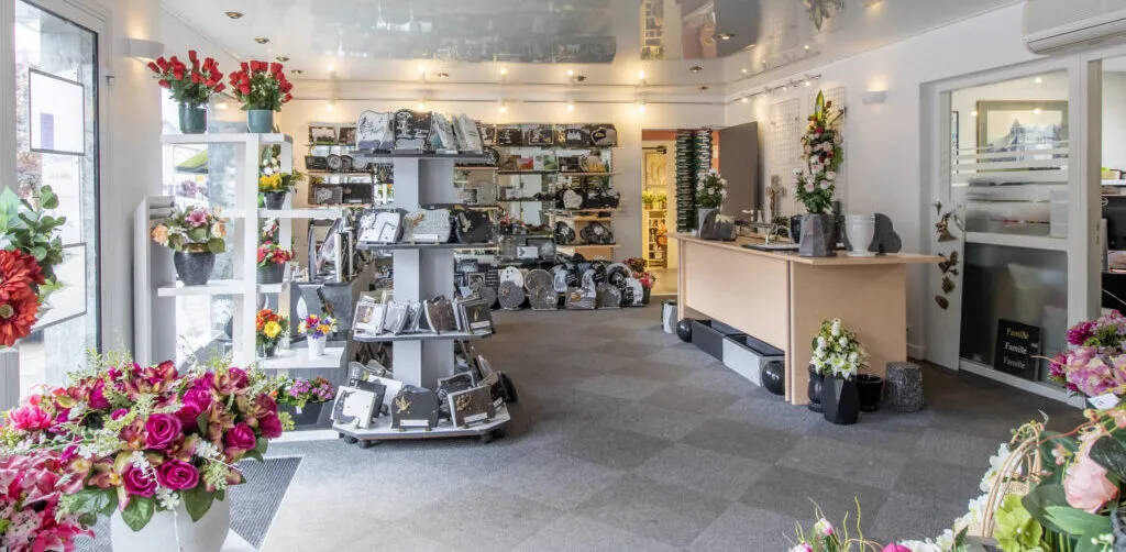 Magasin de marbrerie funéraire présentant des plaques gravées et des arrangements floraux