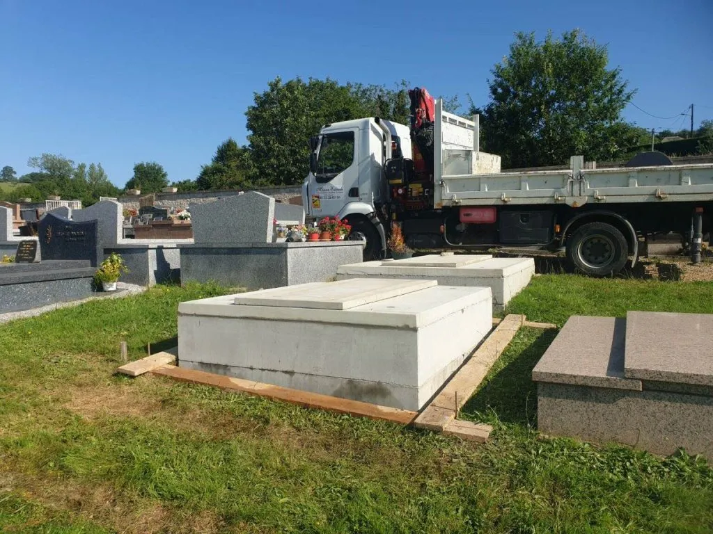 Pose de caveaux funéraires en béton dans un cimetière avec camion-grue en arrière-plan