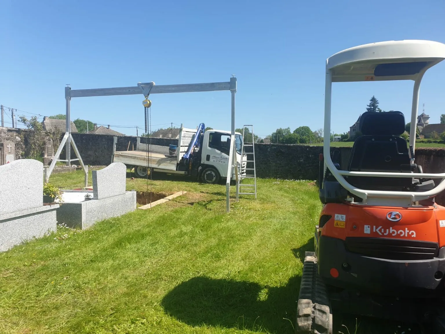 Chantier de marbrerie dans un cimetière avec mini-pelle Kubota et portique de levage