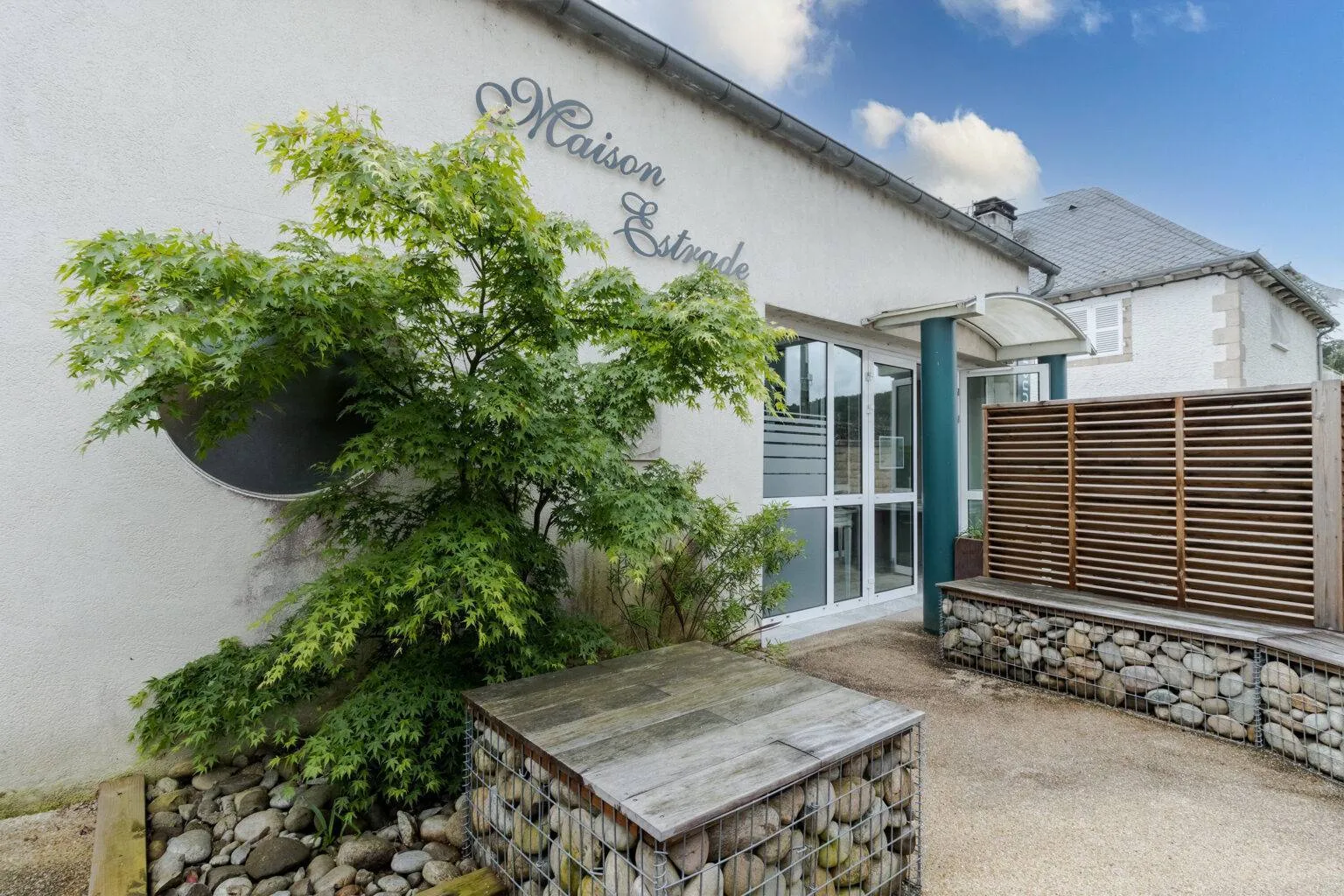 Entrée extérieure de la Maison Estrade bordée de verdure et gabions