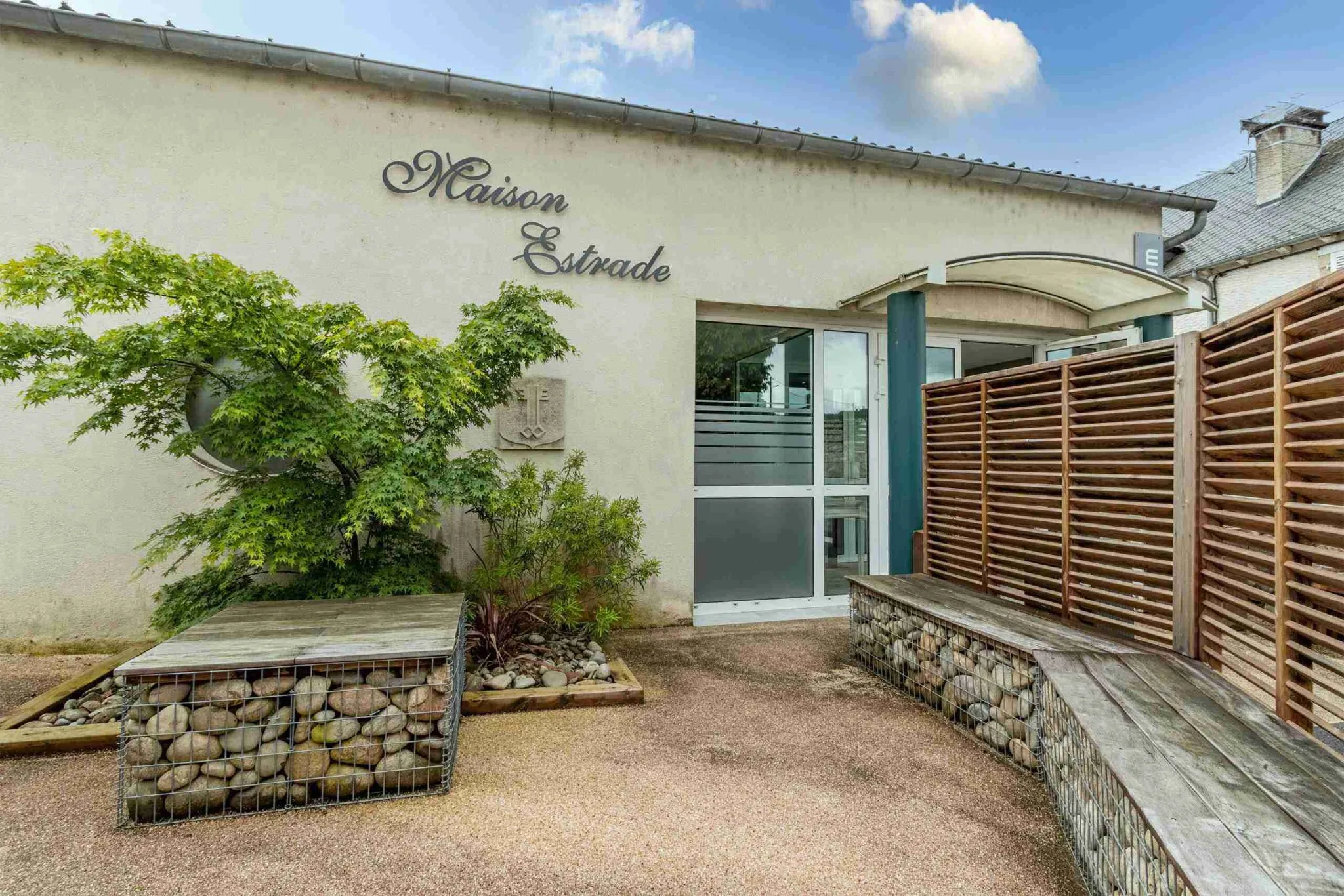 Entrée extérieure de la Maison Estrade bordée de verdure et gabions