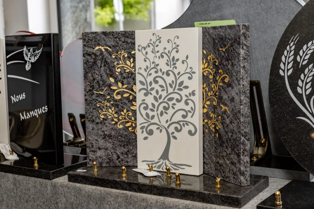 Plaque funéraire en granit sombre ornée d'un panneau central blanc sculpté d'un arbre de vie