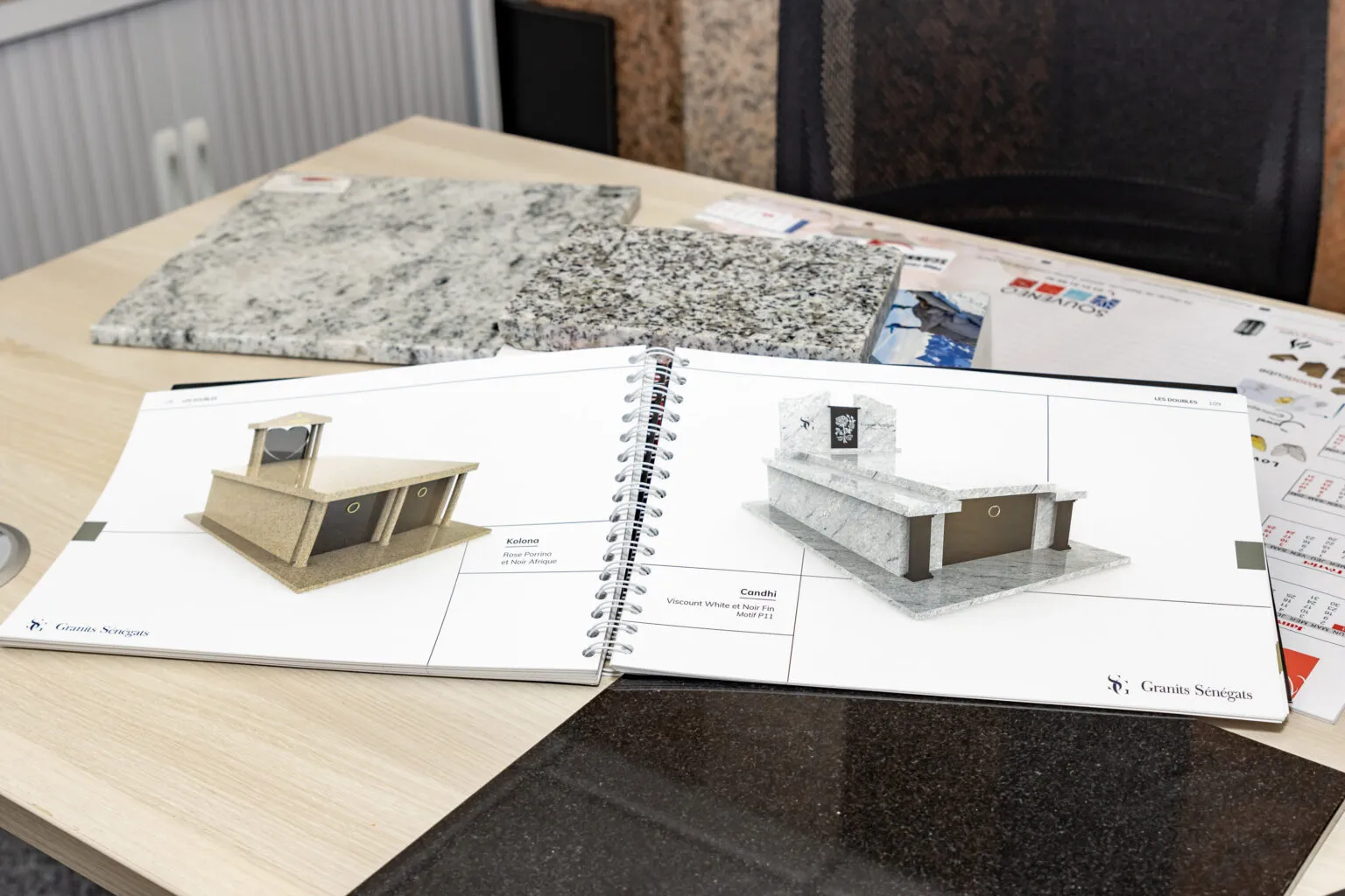 Catalogue de monuments funéraires ouvert sur un bureau à côté d'échantillons de granit