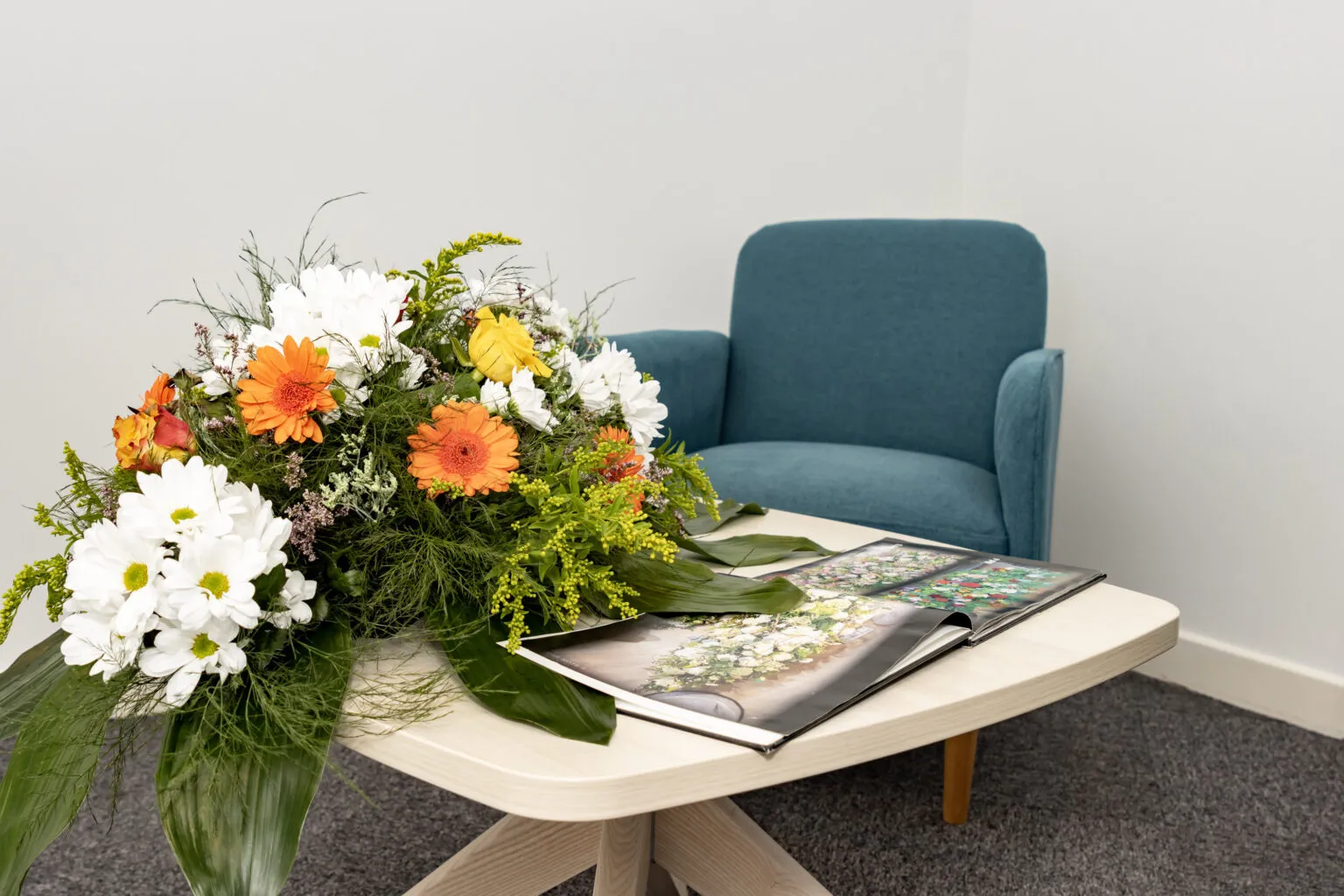 Composition florale et catalogue posés sur une table basse dans un espace de conseil funéraire